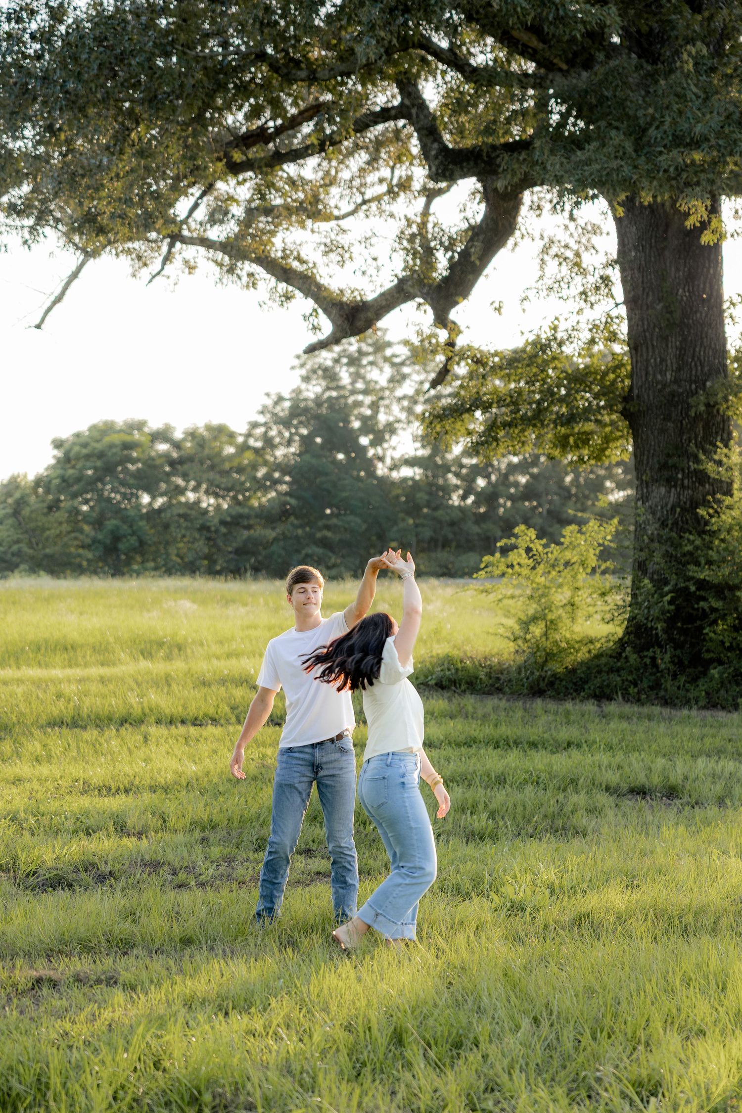 Romantic couple photos in a natural grass field setting with large trees at sunset.