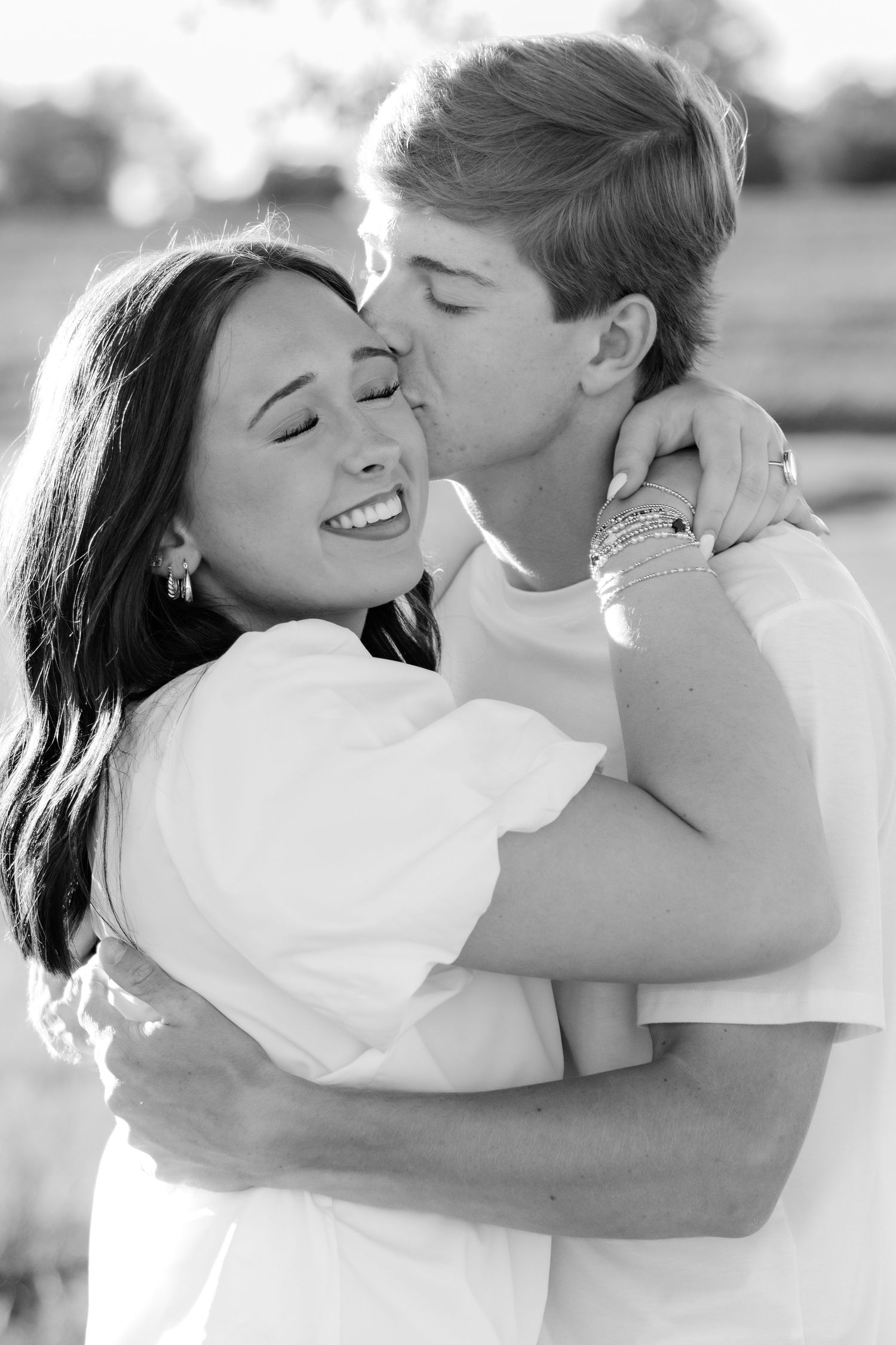 Romantic couple photos in a natural grass field setting with large trees at sunset.