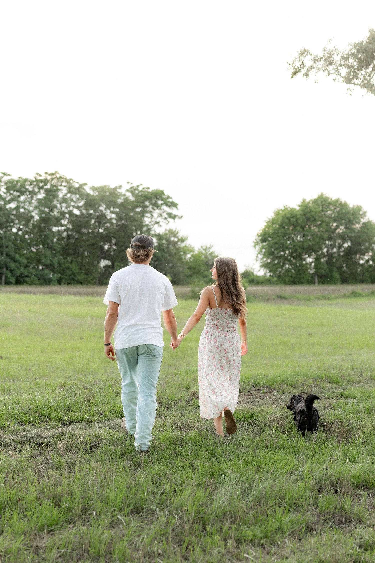 Romantic couple photos in a natural grass field setting with large trees at sunset.