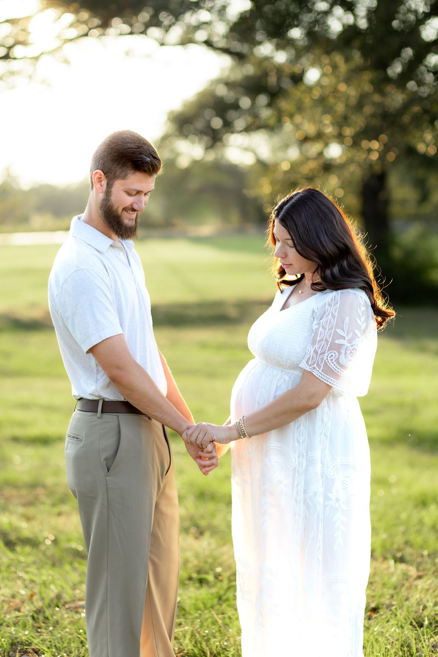 Expecting couple holding hands in a grass field at sunset in Dothan, Alabama