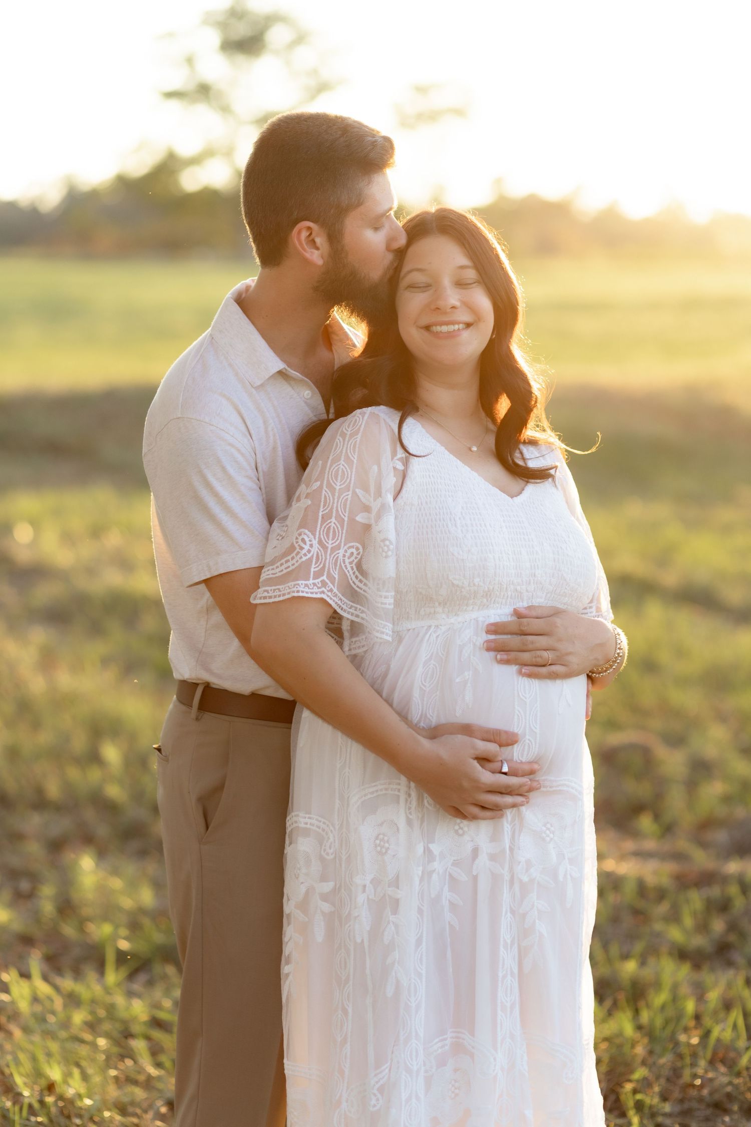 Expecting couple holding each other in a grass field at sunset in Dothan, Alabama