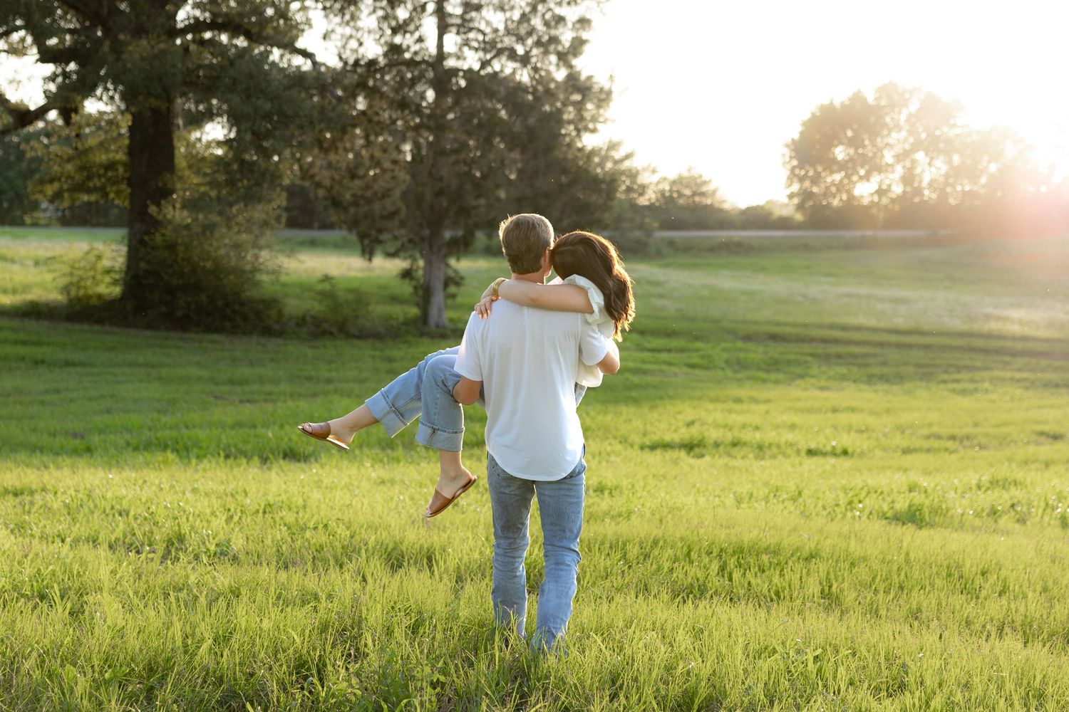 Romantic couple photos in a natural grass field setting with large trees at sunset.