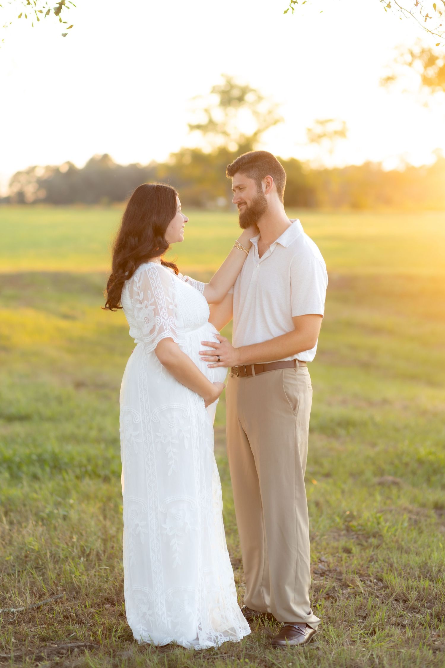 Expecting couple holding each other in a grass field at sunset in Dothan, Alabama