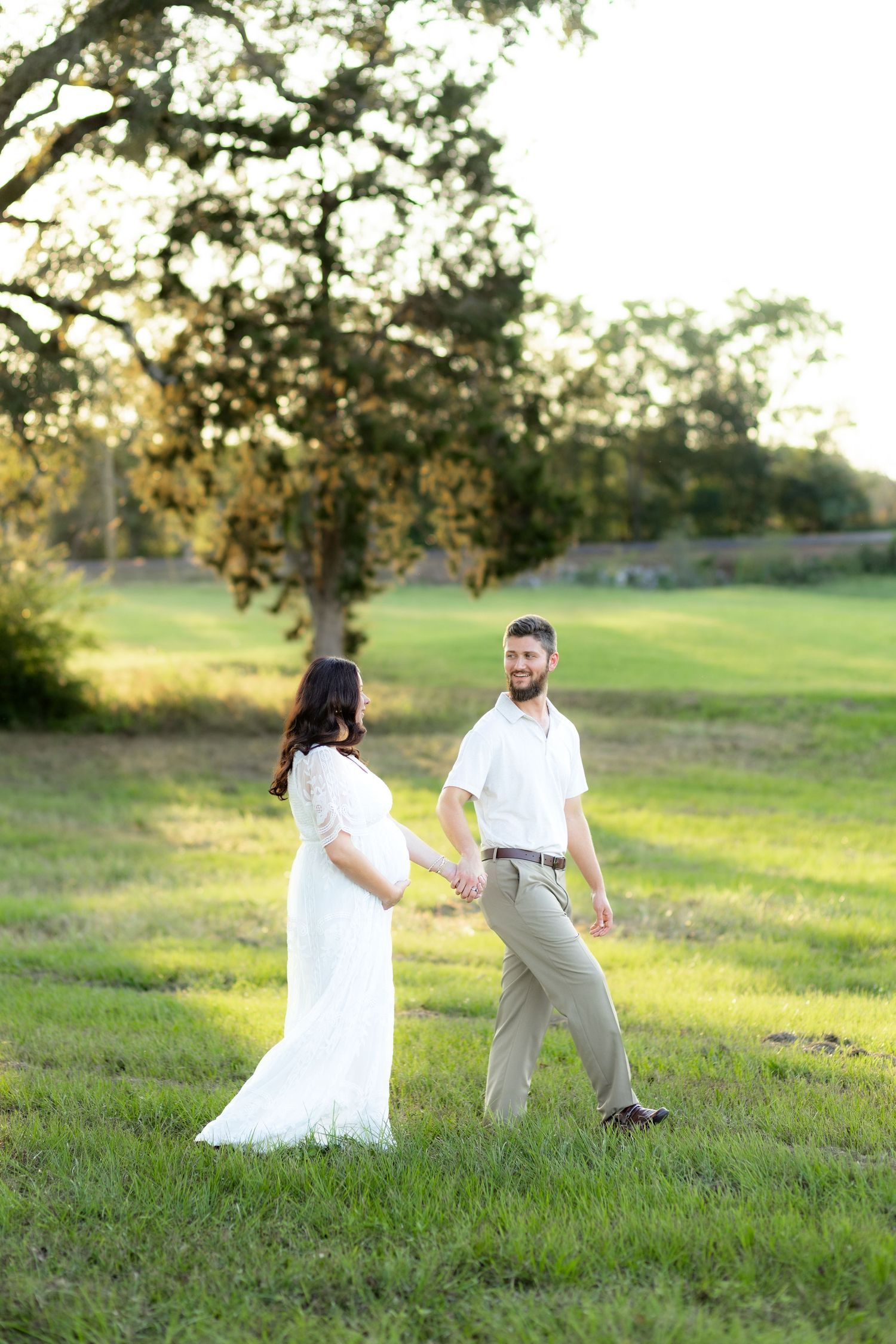 Expecting couple walking in a grass field at sunset in Dothan, Alabama