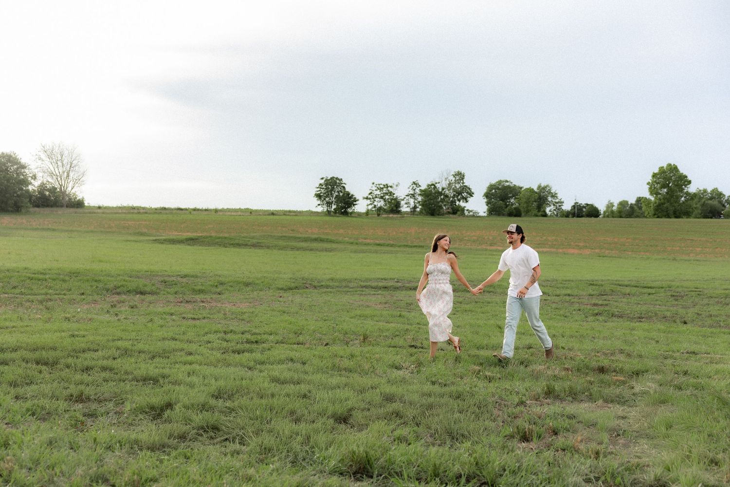Romantic couple photos in a natural grass field setting with large trees at sunset.