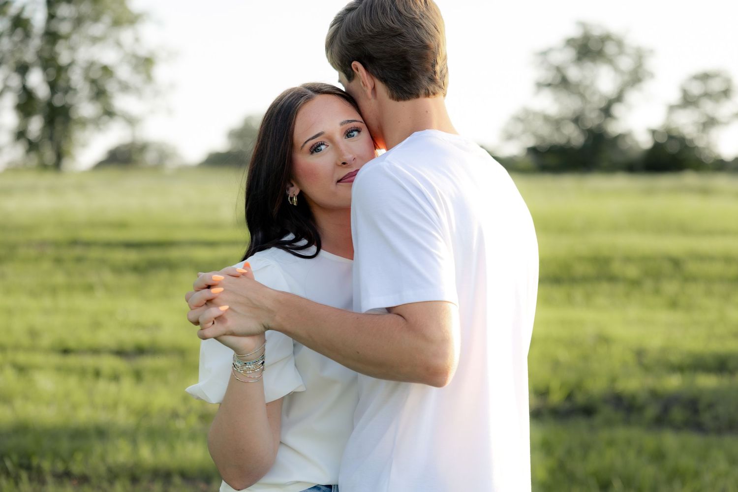 Romantic couple photos in a natural grass field setting with large trees at sunset.
