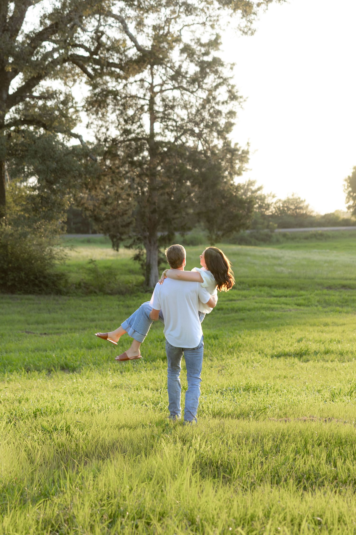 Romantic couple photos in a natural grass field setting with large trees at sunset.