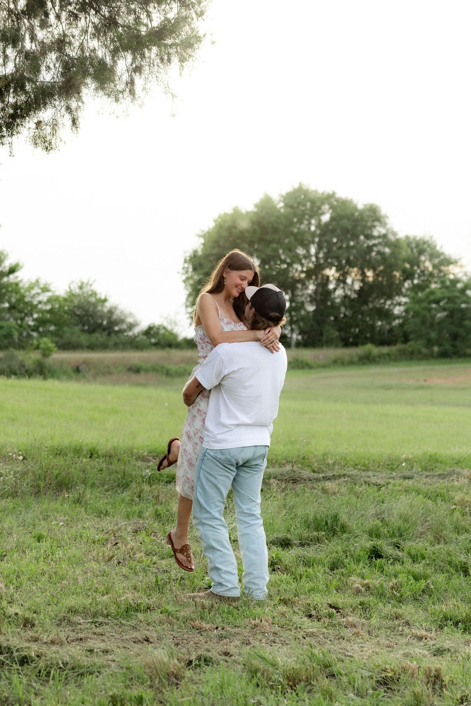 Romantic couple photos in a natural grass field setting with large trees at sunset.