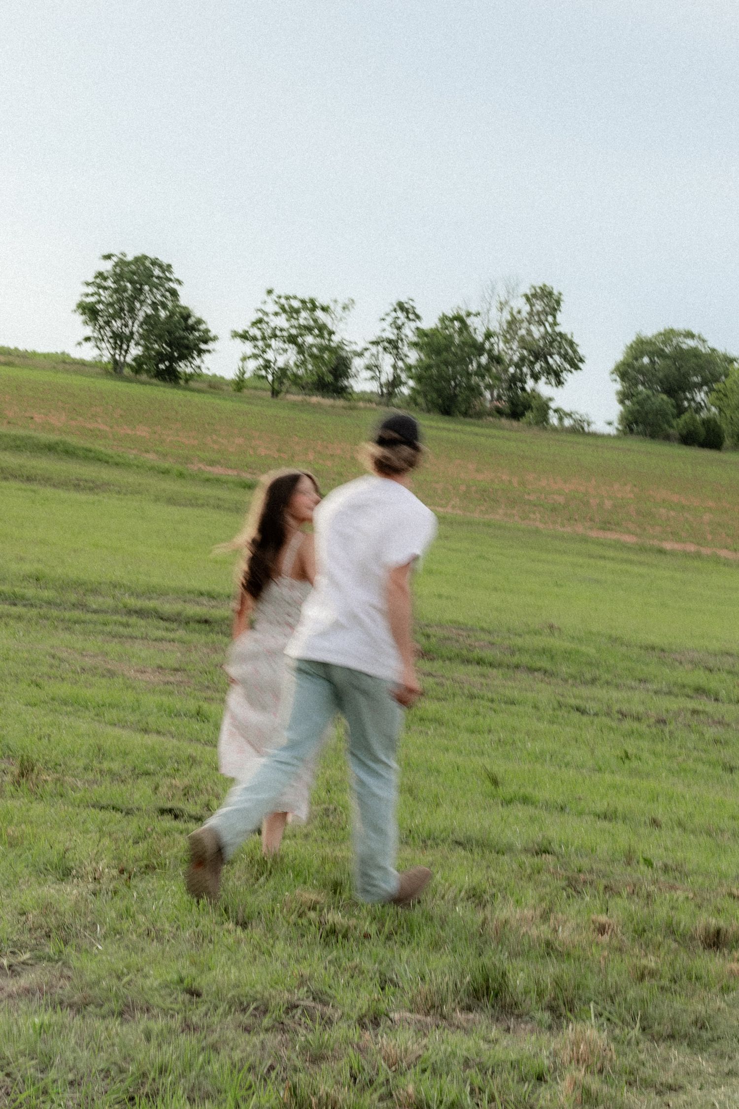 Romantic couple photos in a natural grass field setting with large trees at sunset.