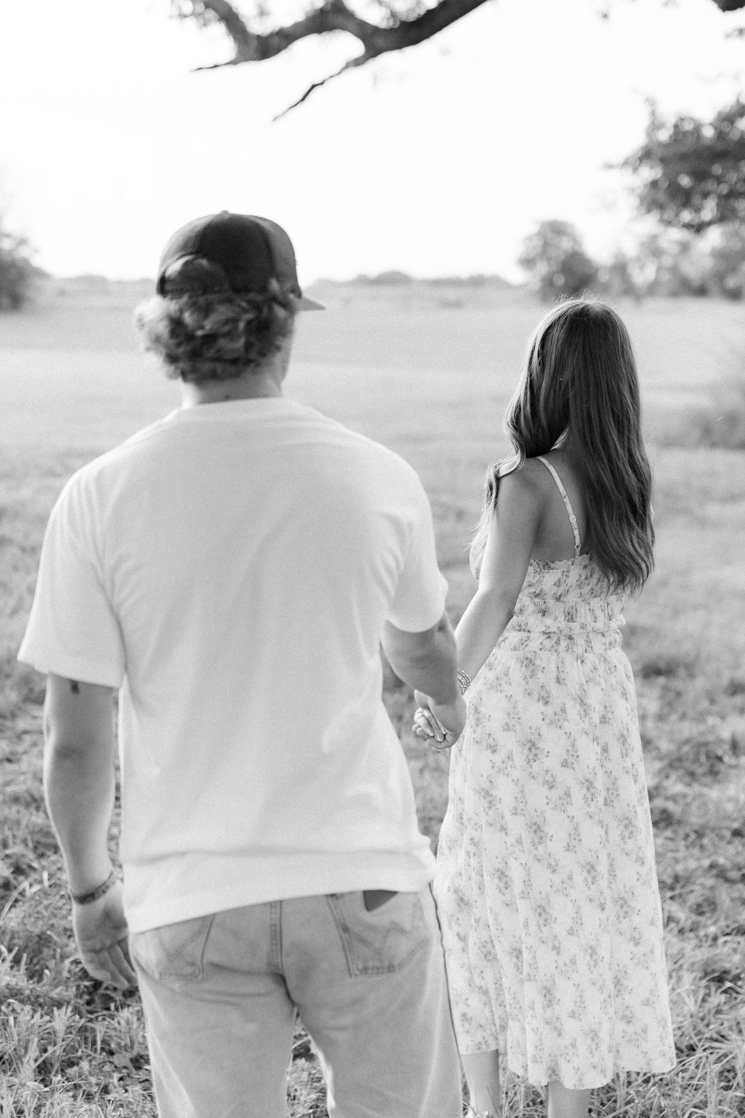 Romantic couple photos in a natural grass field setting with large trees at sunset.
