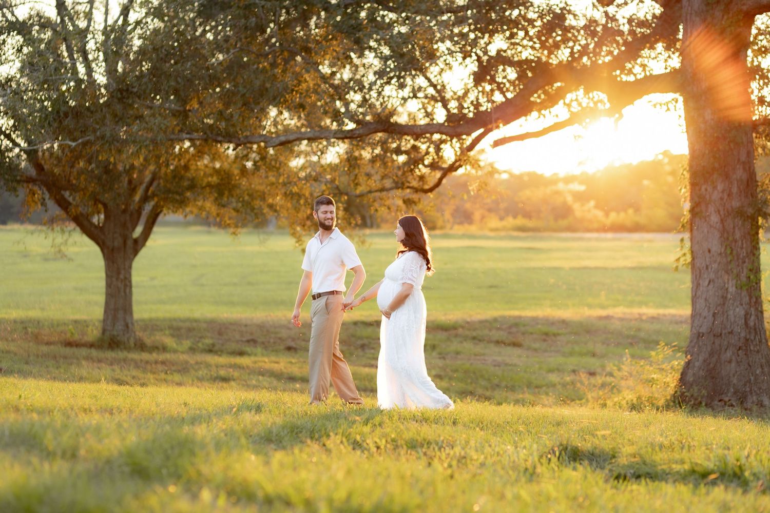 Expecting couple walking in a grass field at sunset in Dothan, Alabama