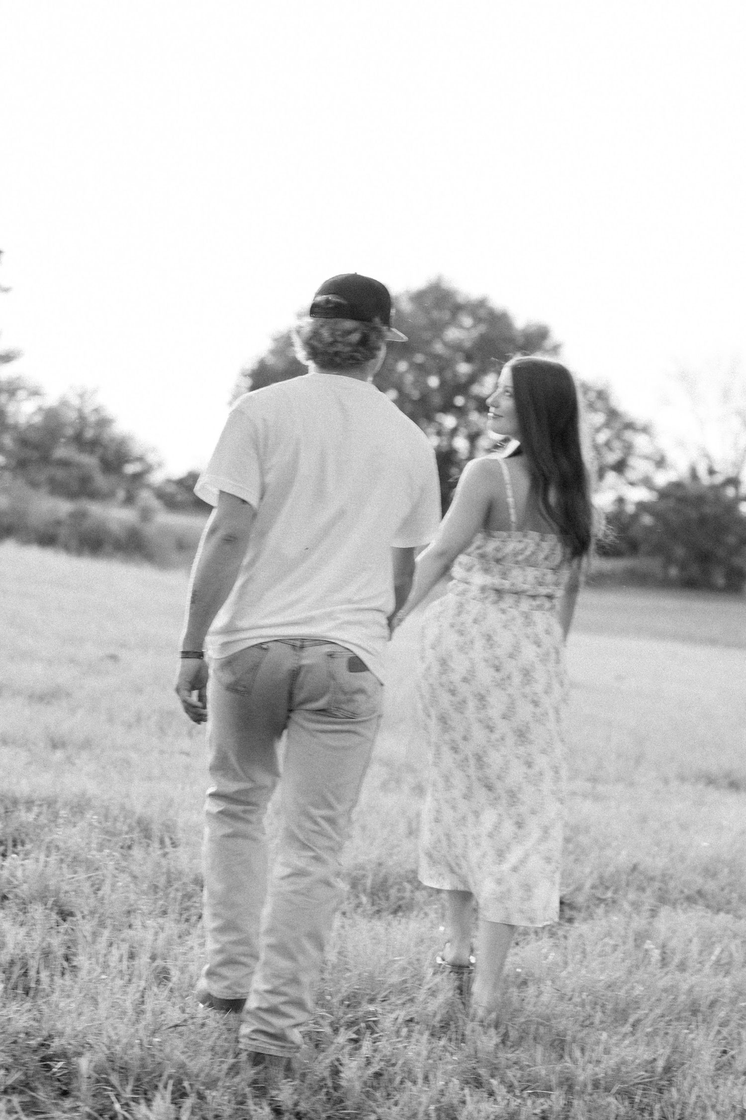 Romantic couple photos in a natural grass field setting with large trees at sunset.