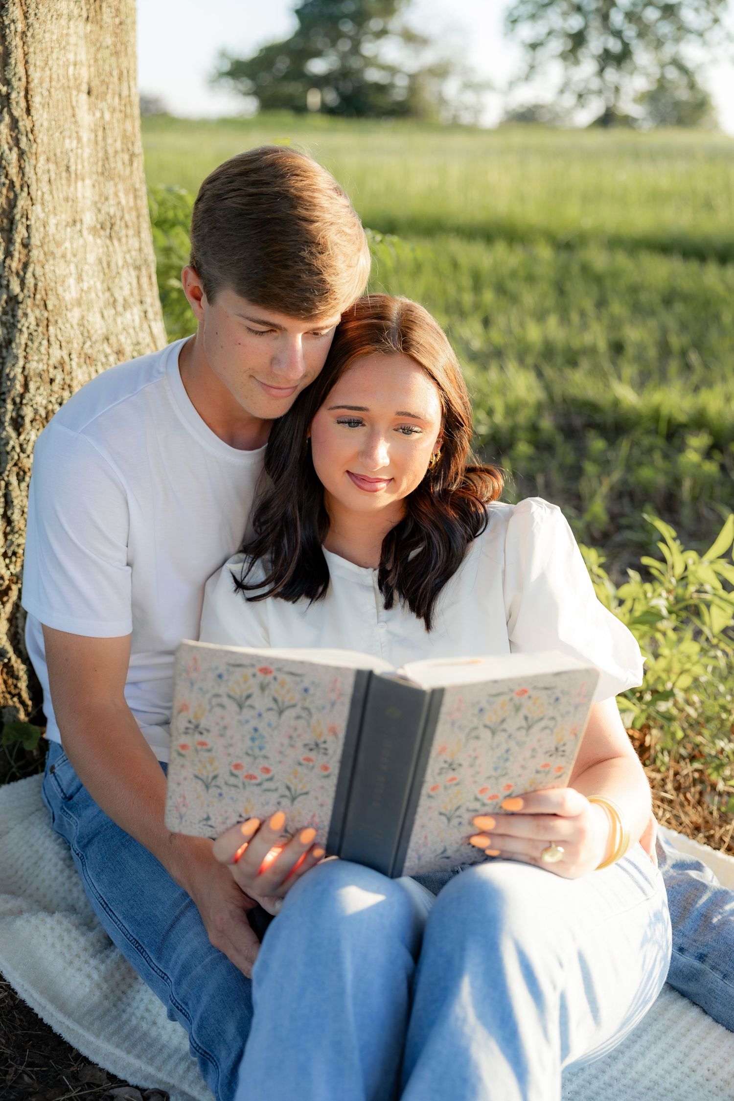 Romantic couple photos in a natural grass field setting with large trees at sunset.