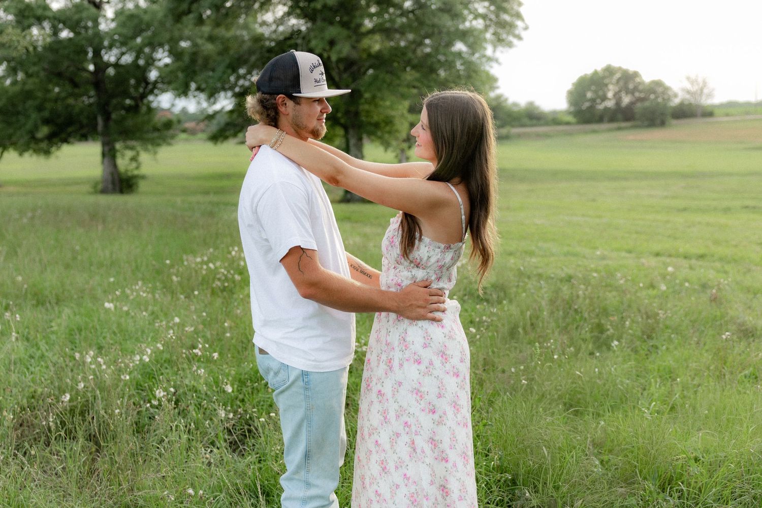 Romantic couple photos in a natural grass field setting with large trees at sunset.