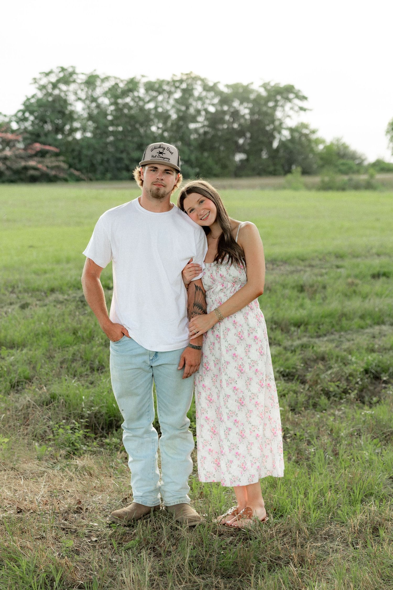 Romantic couple photos in a natural grass field setting with large trees at sunset.