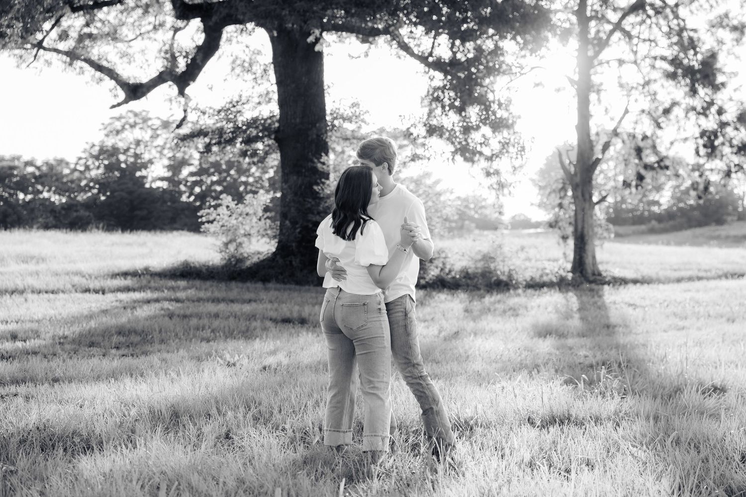 Romantic couple photos in a natural grass field setting with large trees at sunset.