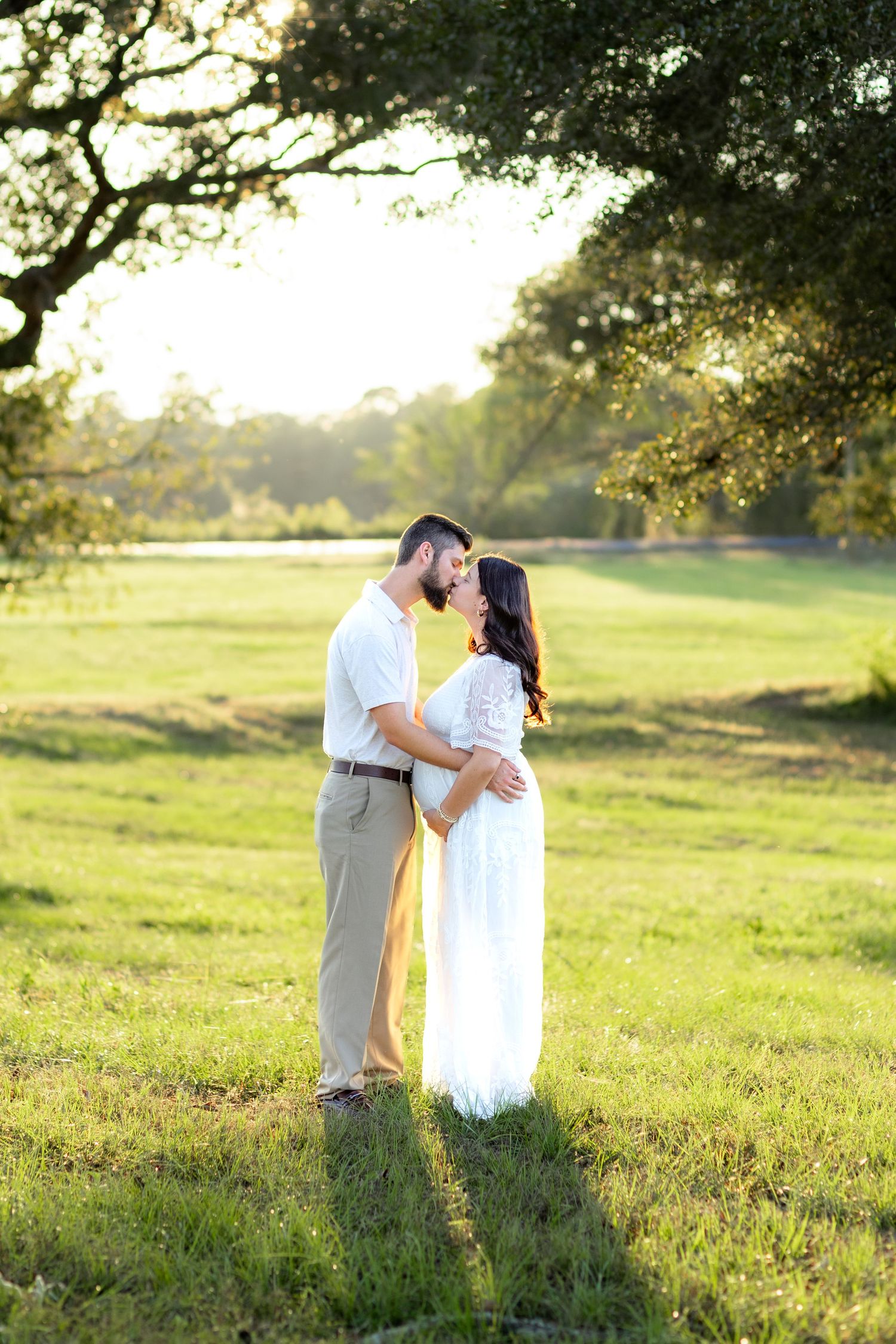 Expecting couple holding each other in a grass field at sunset in Dothan, Alabama