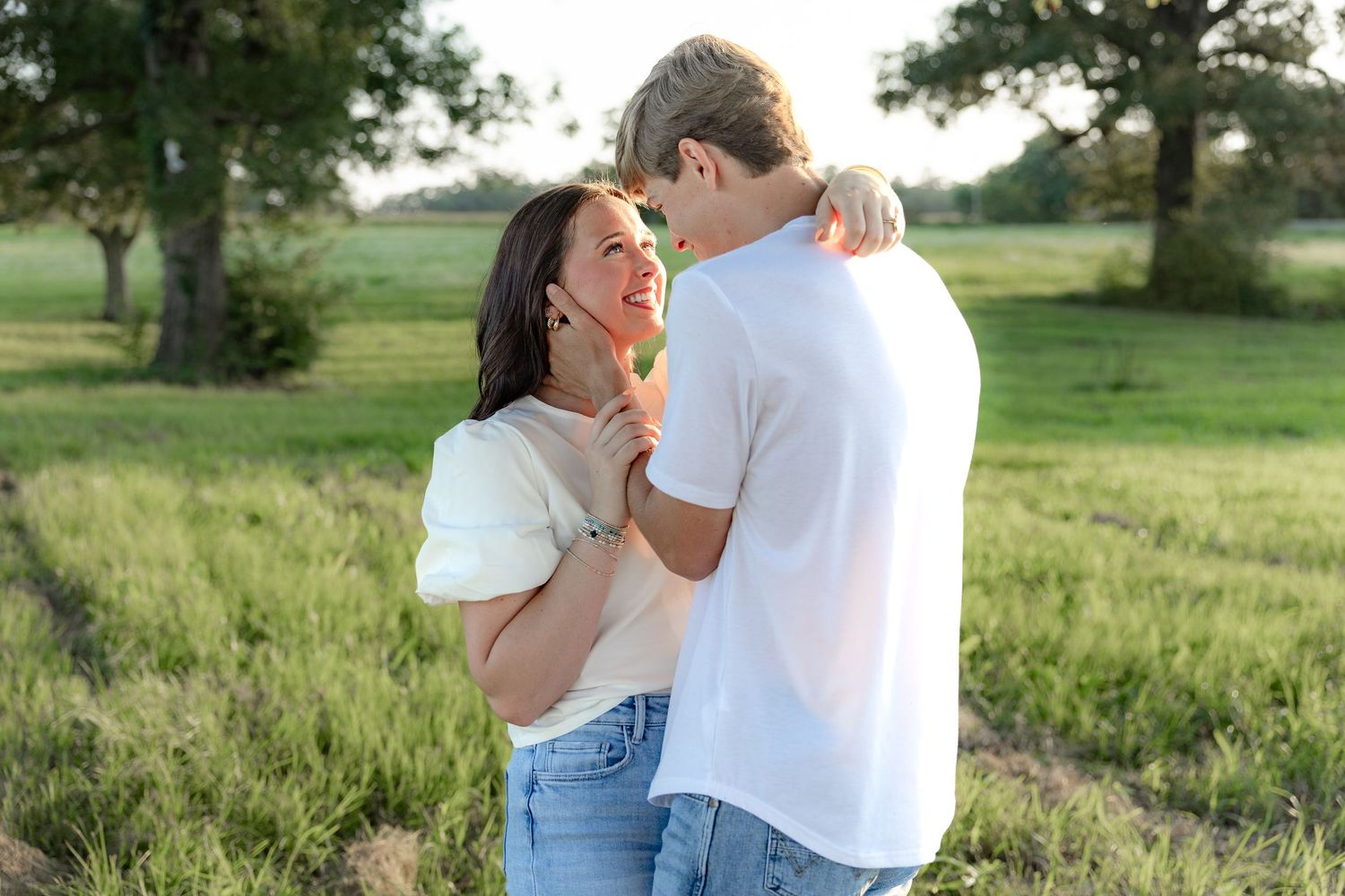 Romantic couple photos in a natural grass field setting with large trees at sunset.