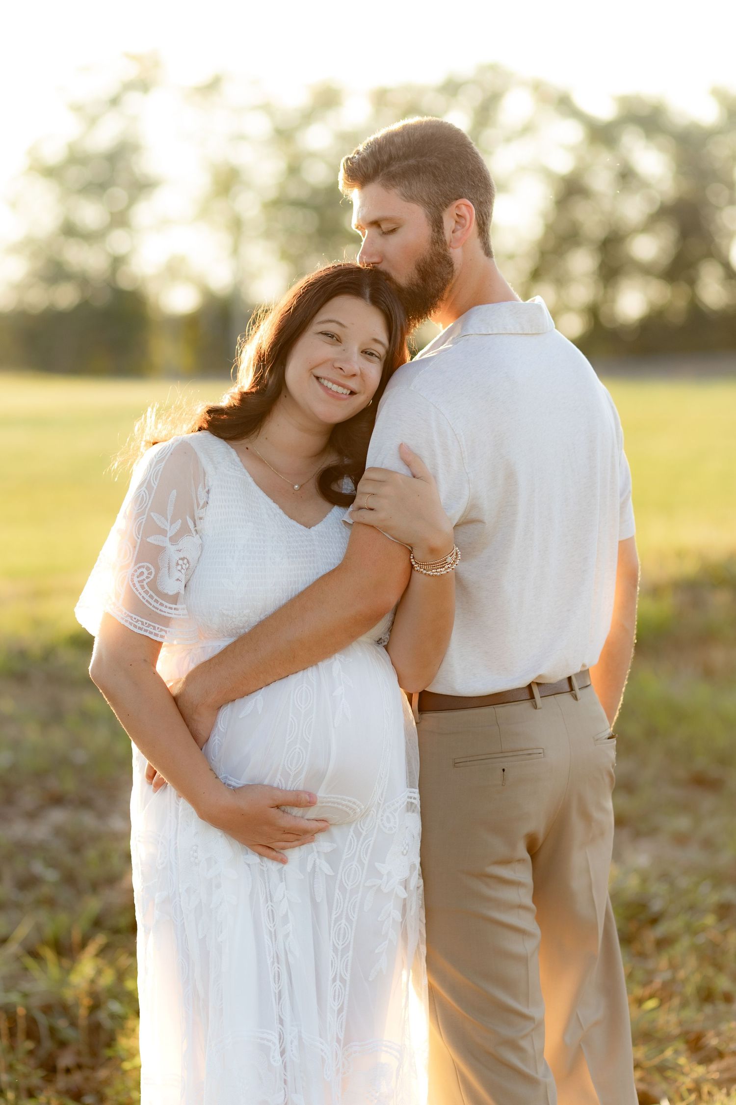 Expecting couple holding each other in a grass field at sunset in Dothan, Alabama