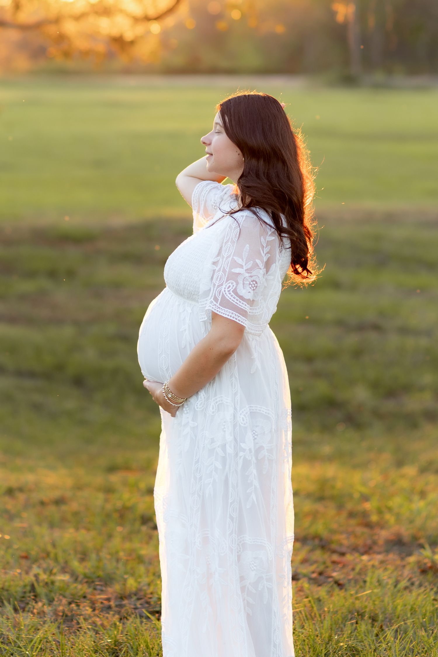 Expecting mother standing in a grass field at sunset in Dothan, Alabama