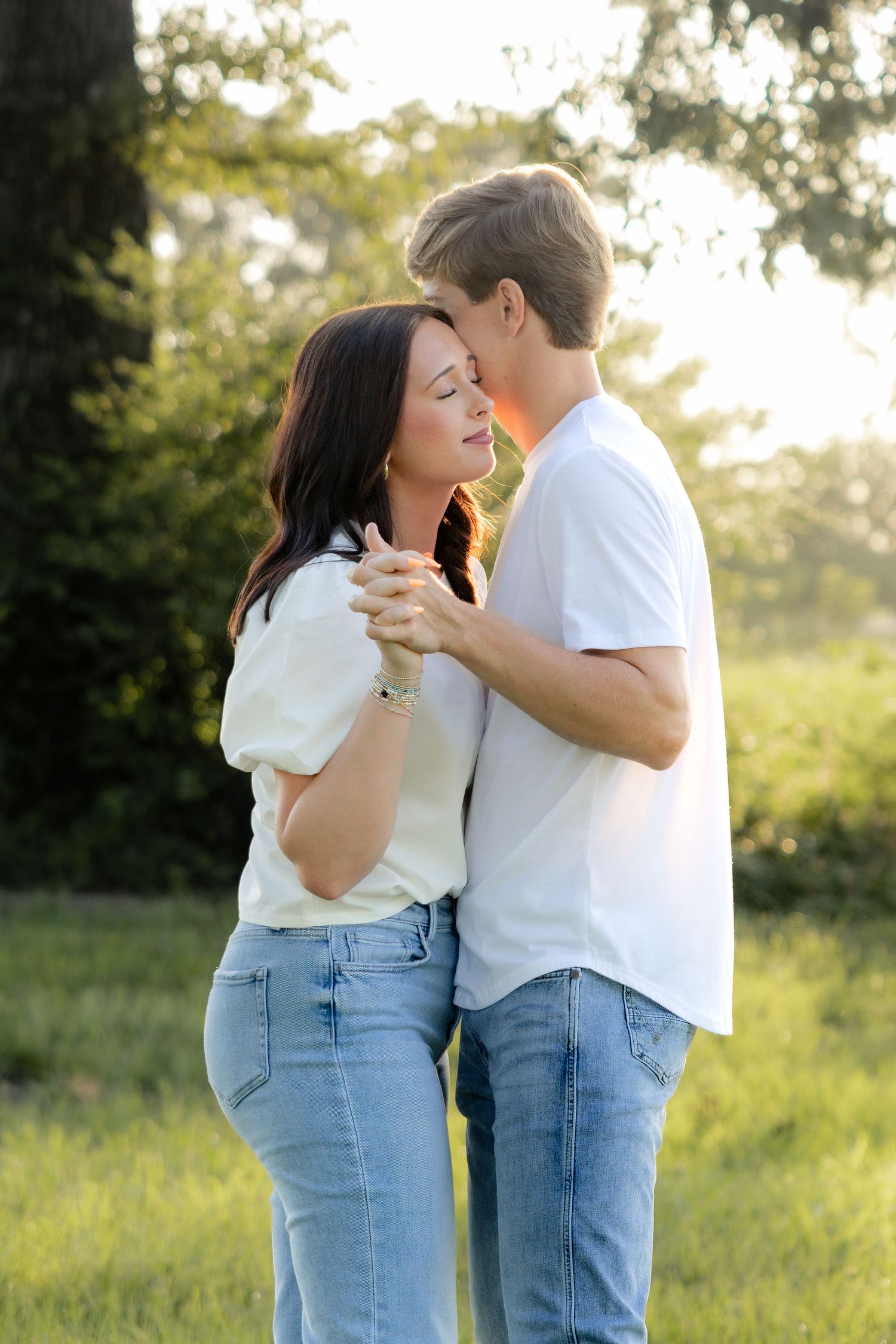 Romantic couple photos in a natural grass field setting with large trees at sunset.