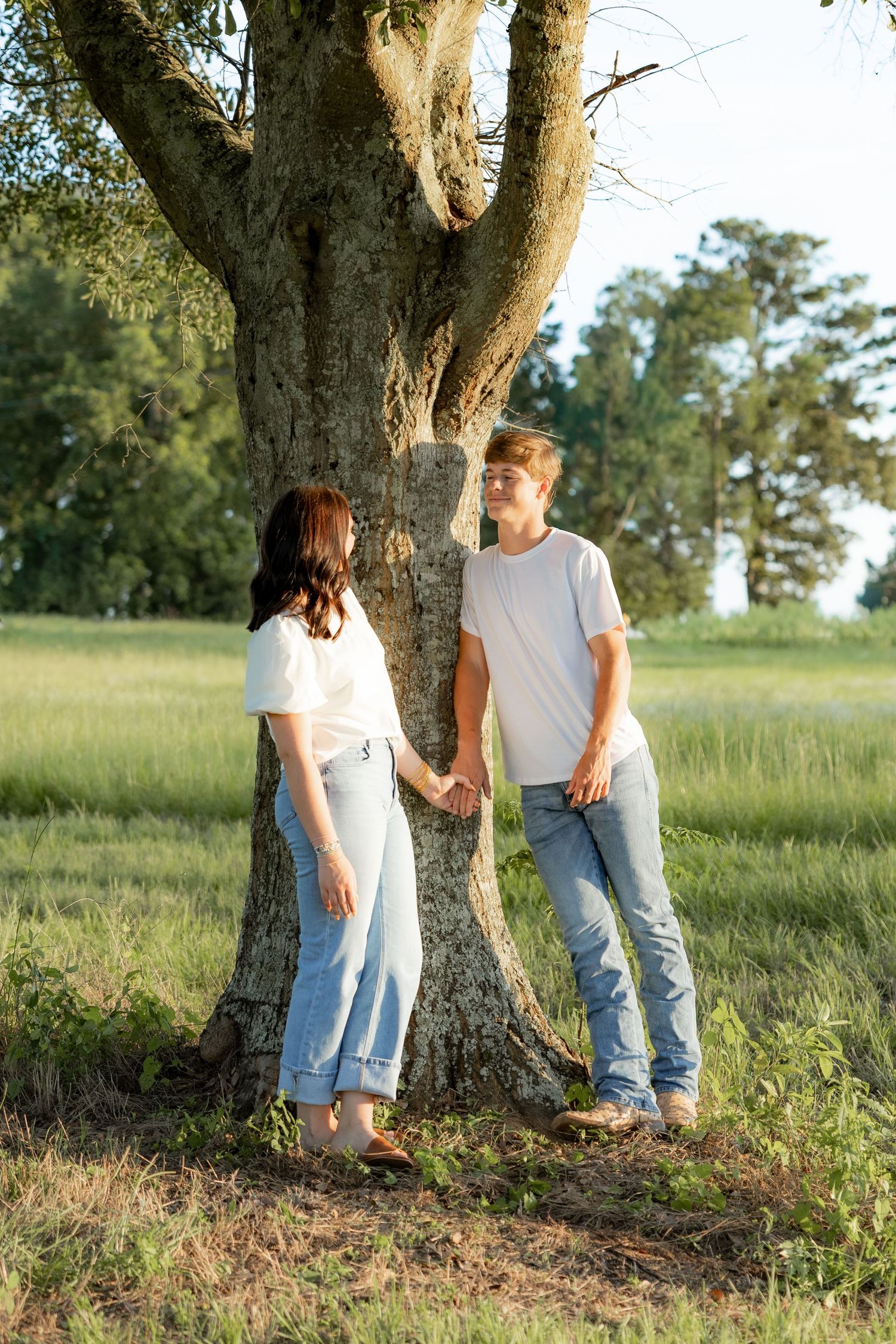 Romantic couple photos in a natural grass field setting with large trees at sunset.