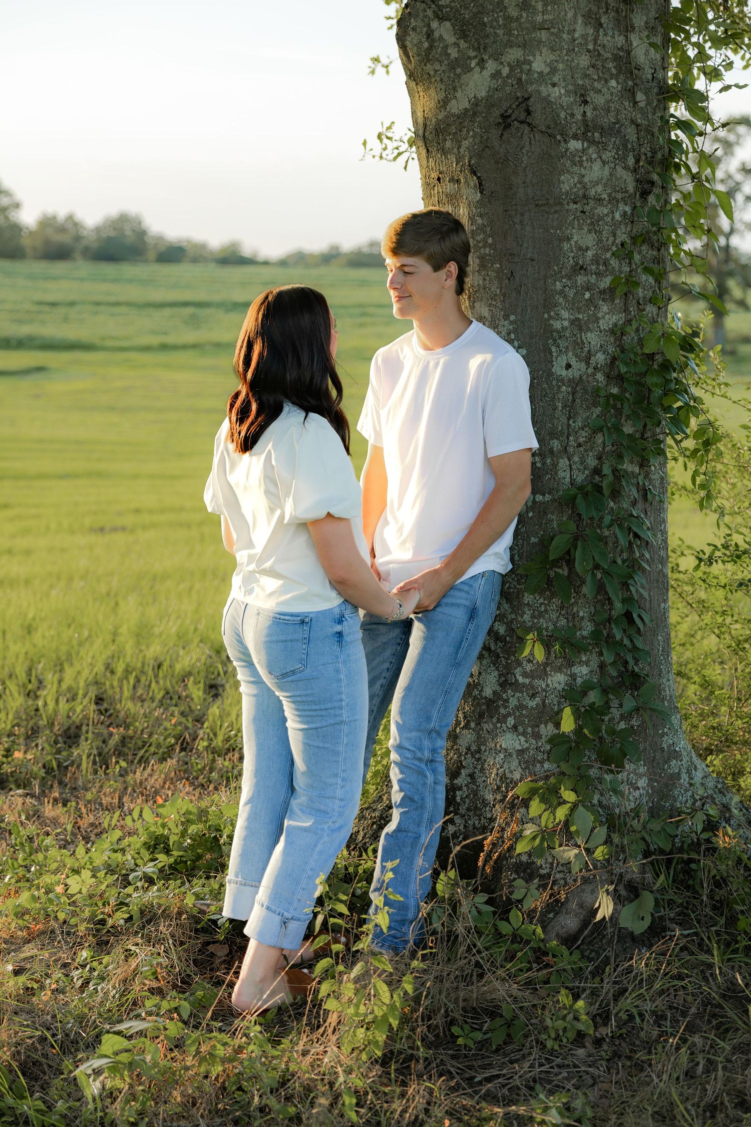 Romantic couple photos in a natural grass field setting with large trees at sunset.