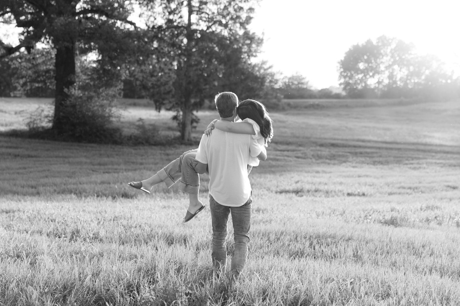 Romantic couple photos in a natural grass field setting with large trees at sunset.