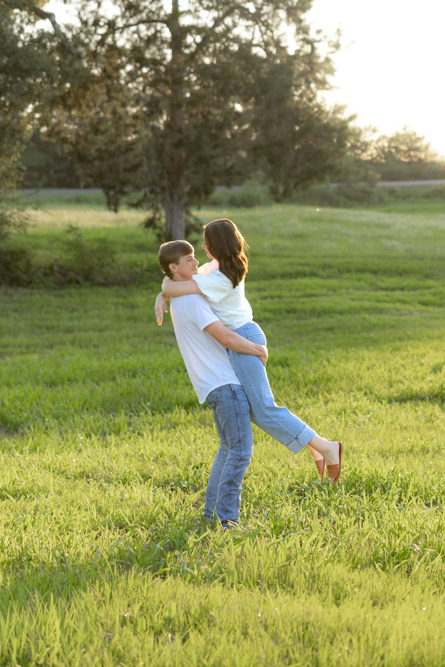 Romantic couple photos in a natural grass field setting with large trees at sunset.