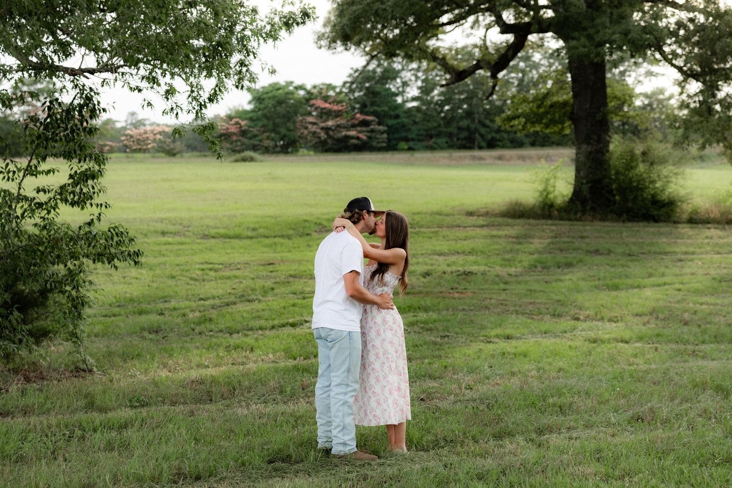 Romantic couple photos in a natural grass field setting with large trees at sunset.