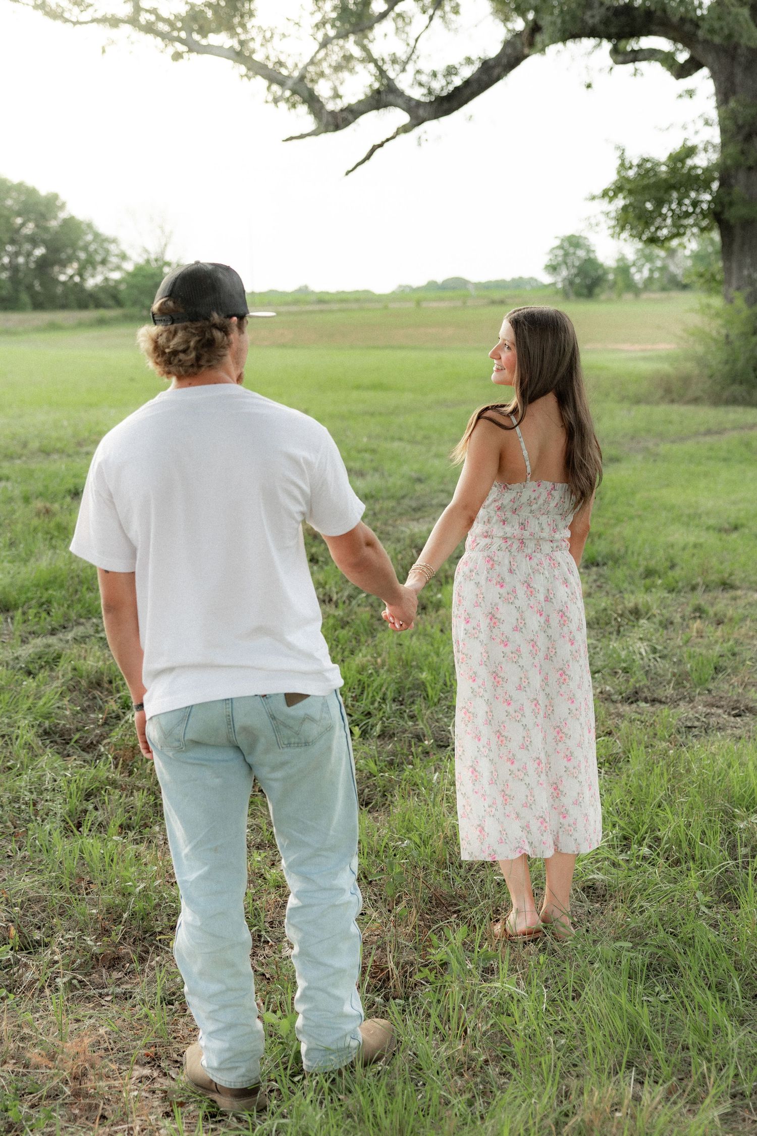 Romantic couple photos in a natural grass field setting with large trees at sunset.