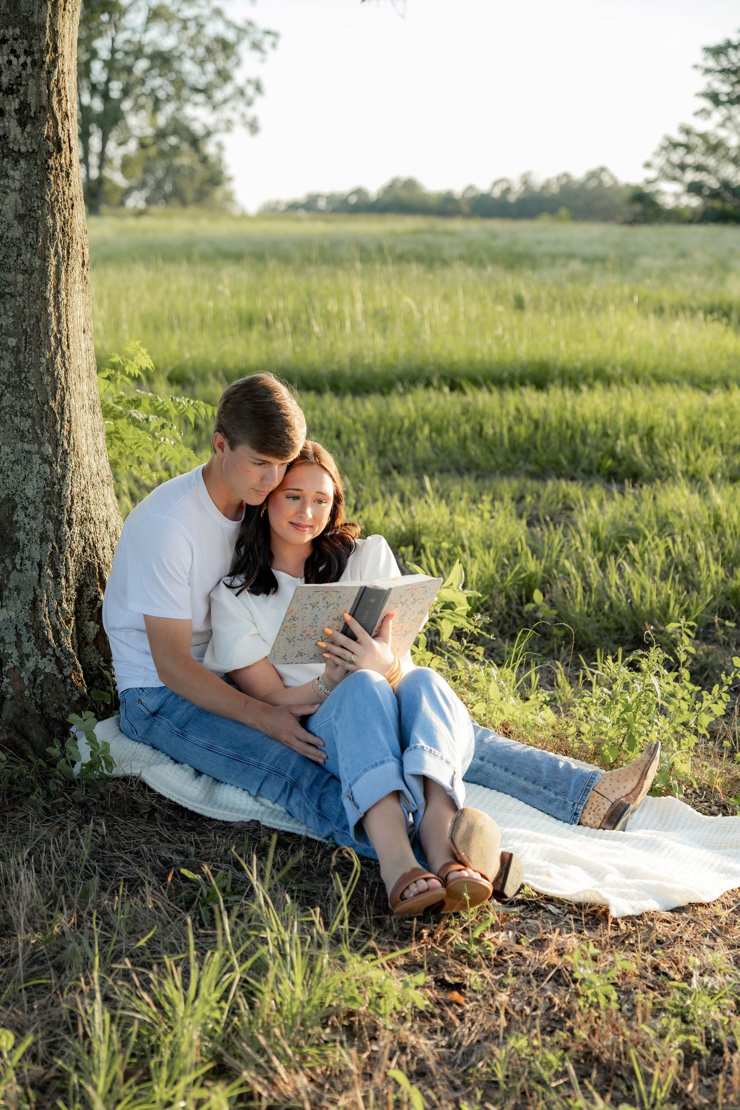 Romantic couple photos in a natural grass field setting with large trees at sunset.