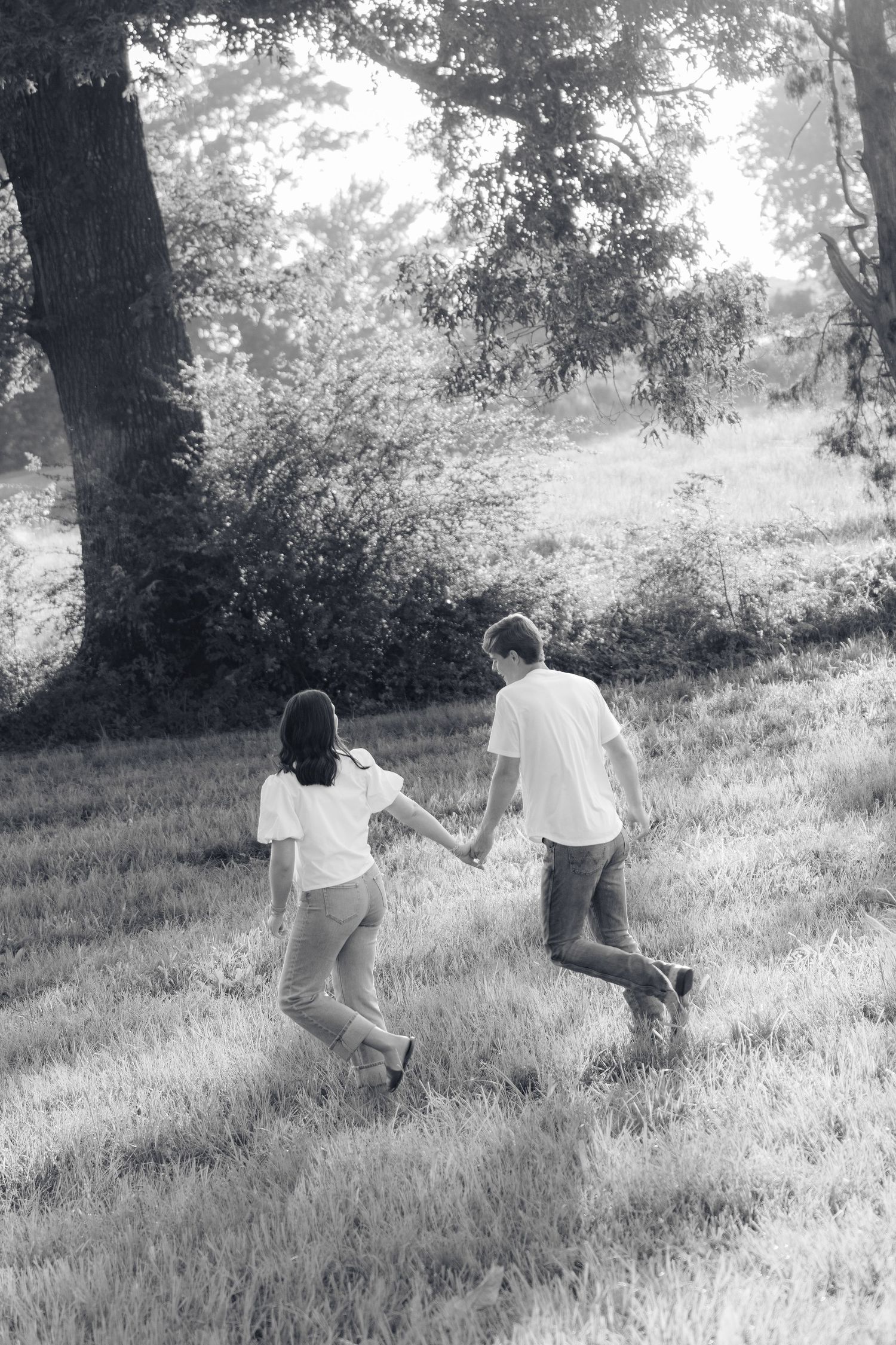 Romantic couple photos in a natural grass field setting with large trees at sunset.