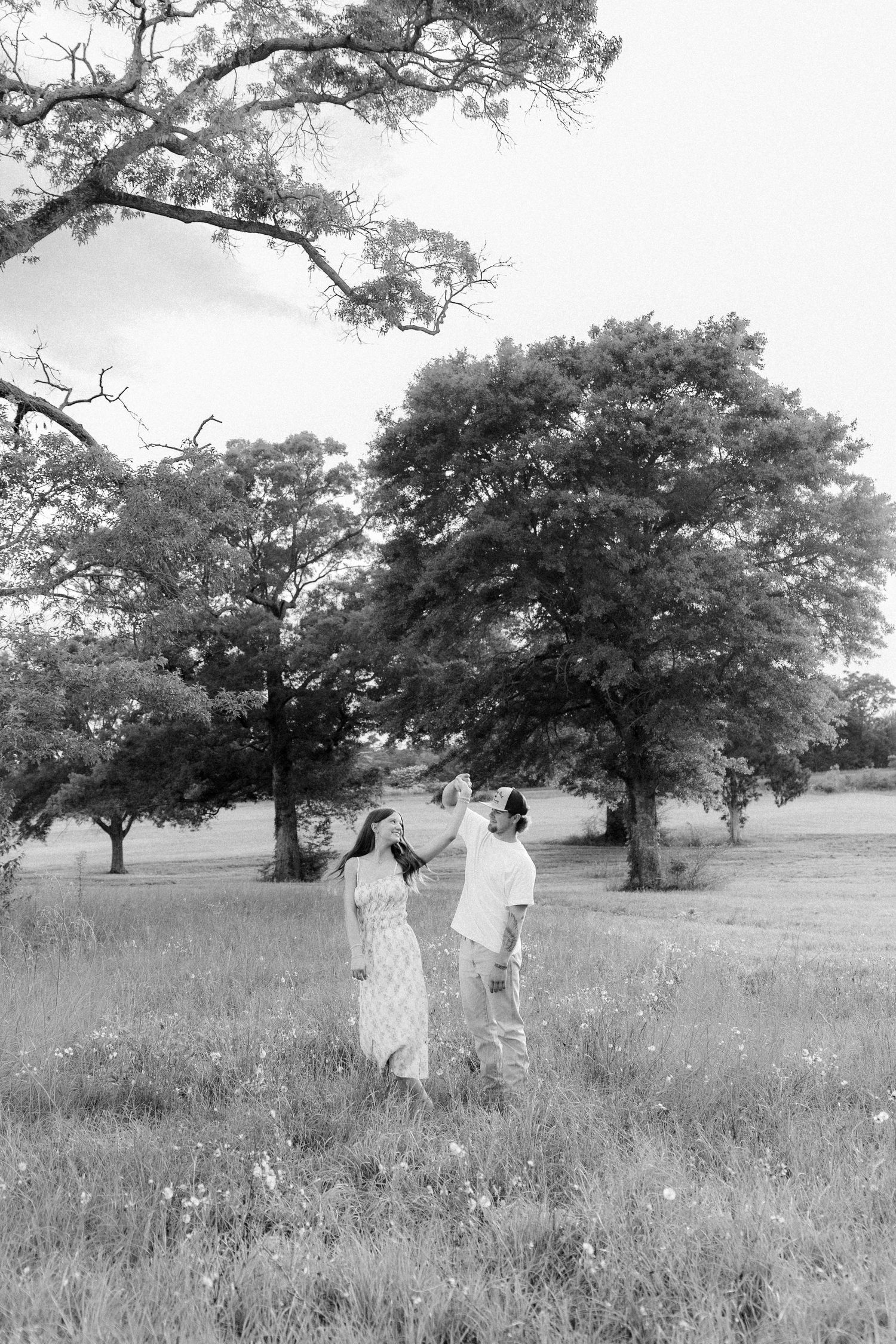 Romantic couple photos in a natural grass field setting with large trees at sunset.