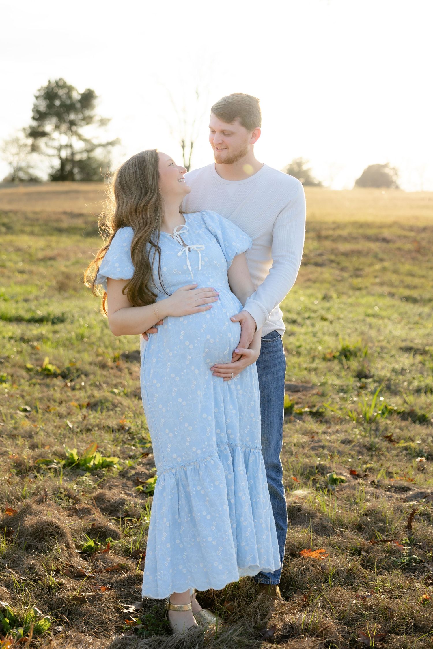 Expecting couple holding each other in a field at sunset in Dothan, Alabama