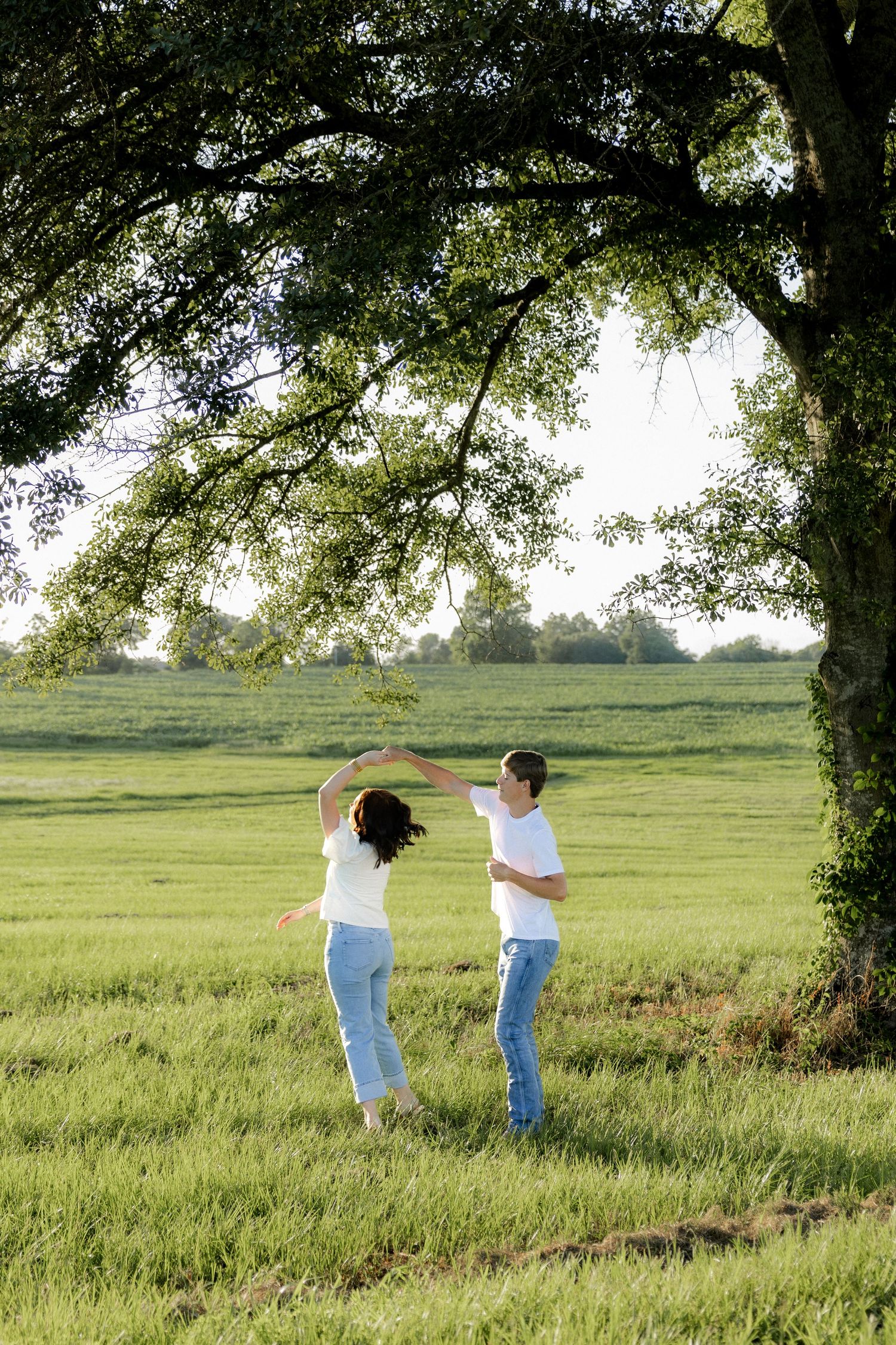 Romantic couple photos in a natural grass field setting with large trees at sunset.
