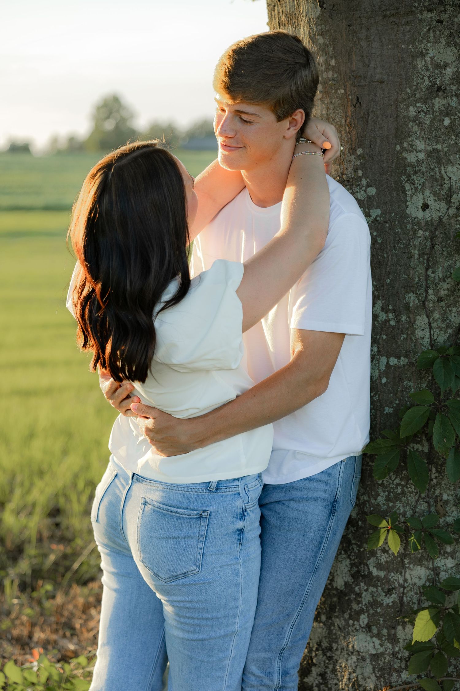 Romantic couple photos in a natural grass field setting with large trees at sunset.