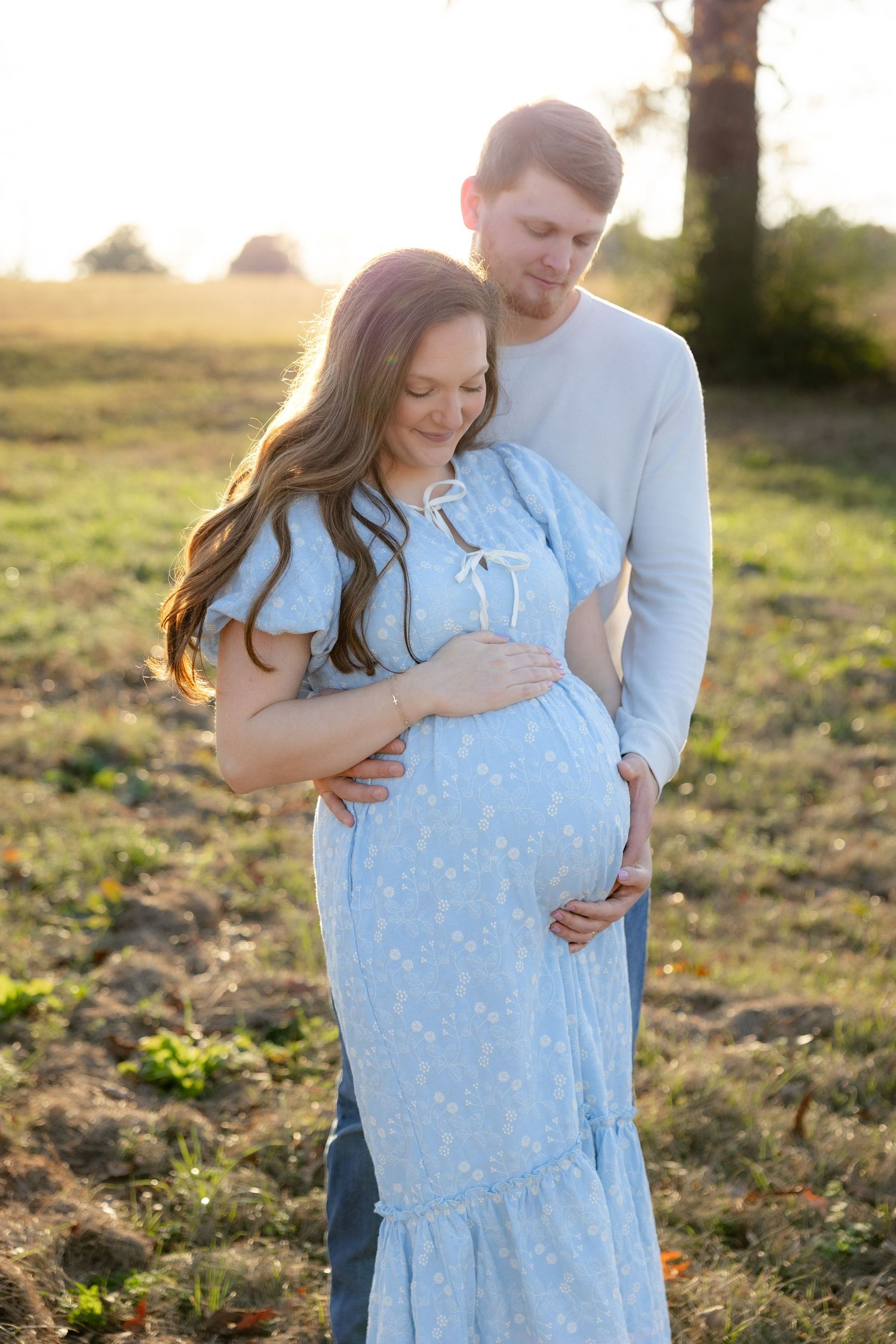 Expecting couple holding each other in a field at sunset in Dothan, Alabama
