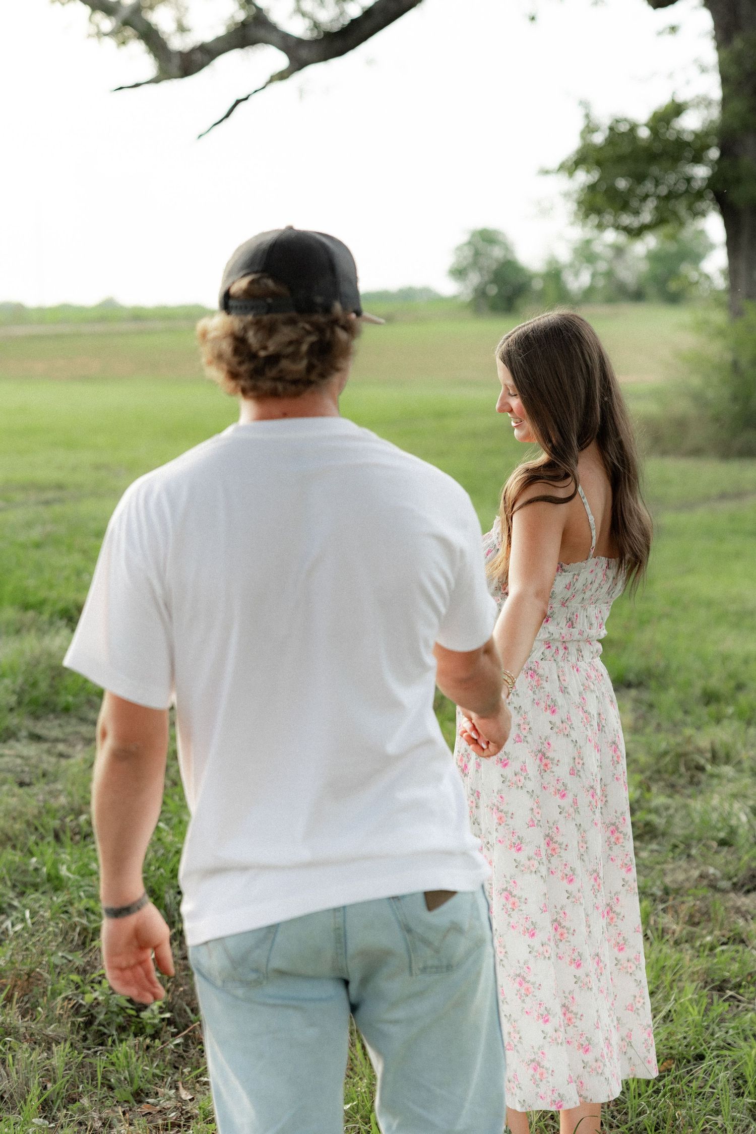 Romantic couple photos in a natural grass field setting with large trees at sunset.