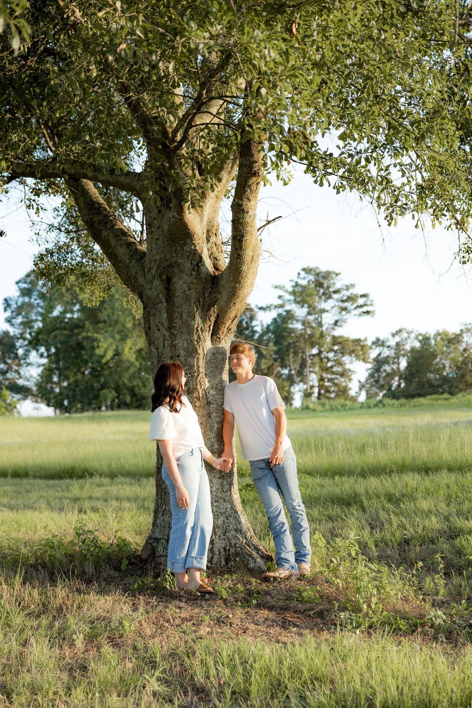 Romantic couple photos in a natural grass field setting with large trees at sunset.