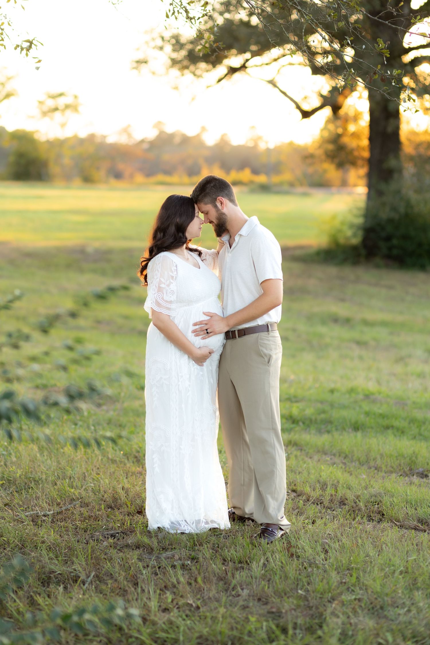Expecting couple holding each other in a grass field at sunset in Dothan, Alabama