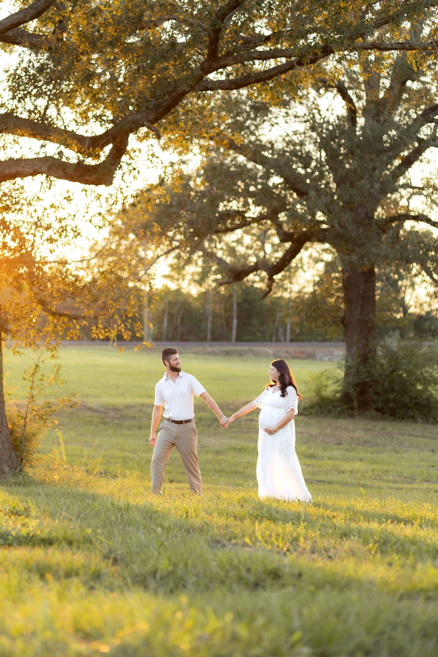 Expecting couple walking in a grass field at sunset in Dothan, Alabama