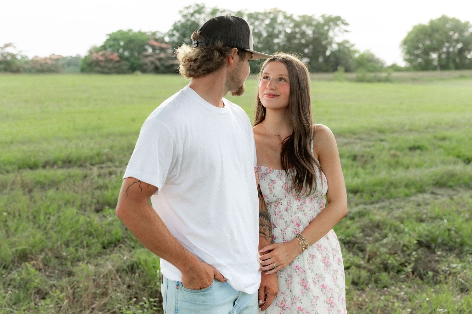 Romantic couple photos in a natural grass field setting with large trees at sunset.