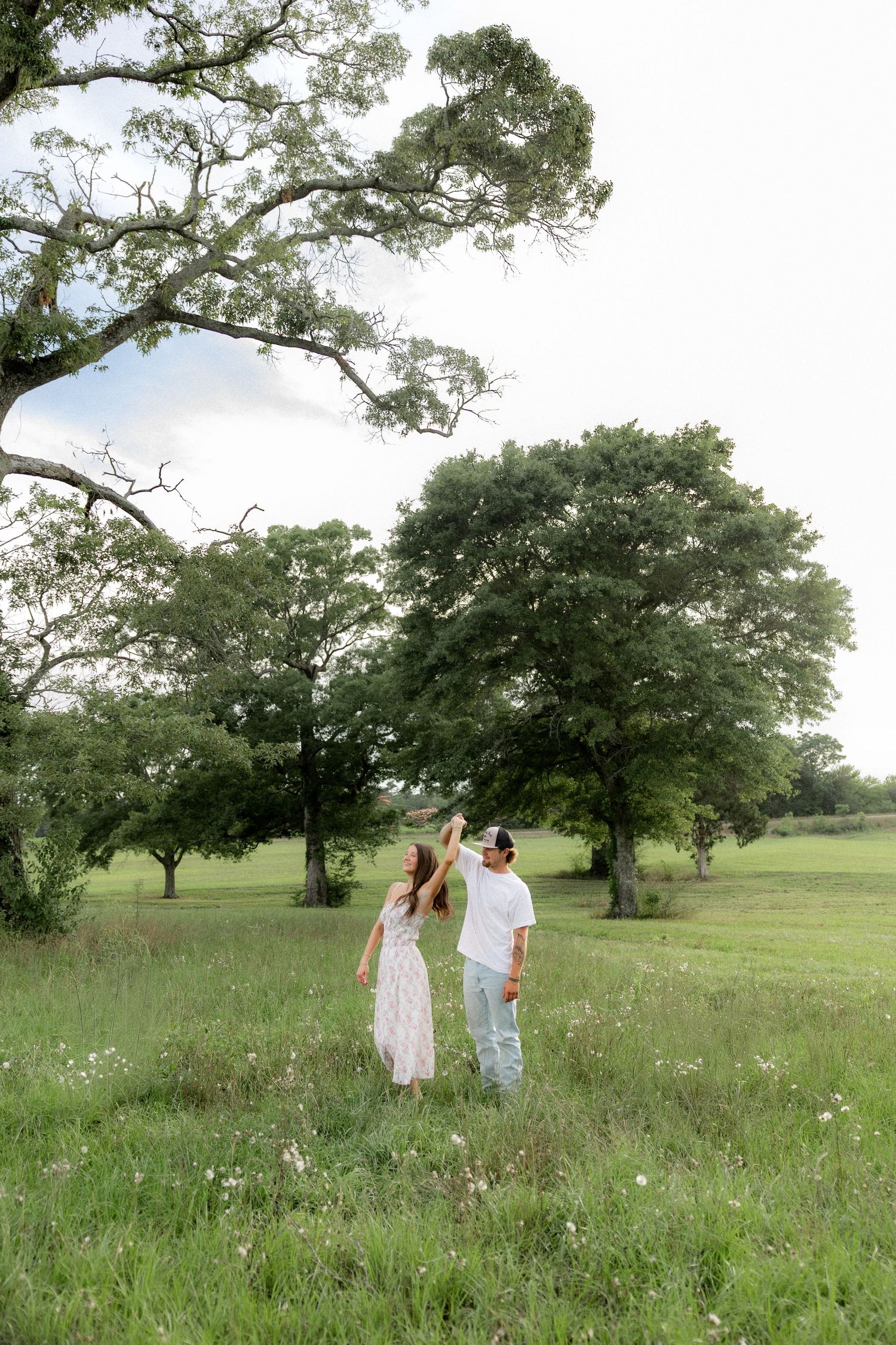 Romantic couple photos in a natural grass field setting with large trees at sunset.