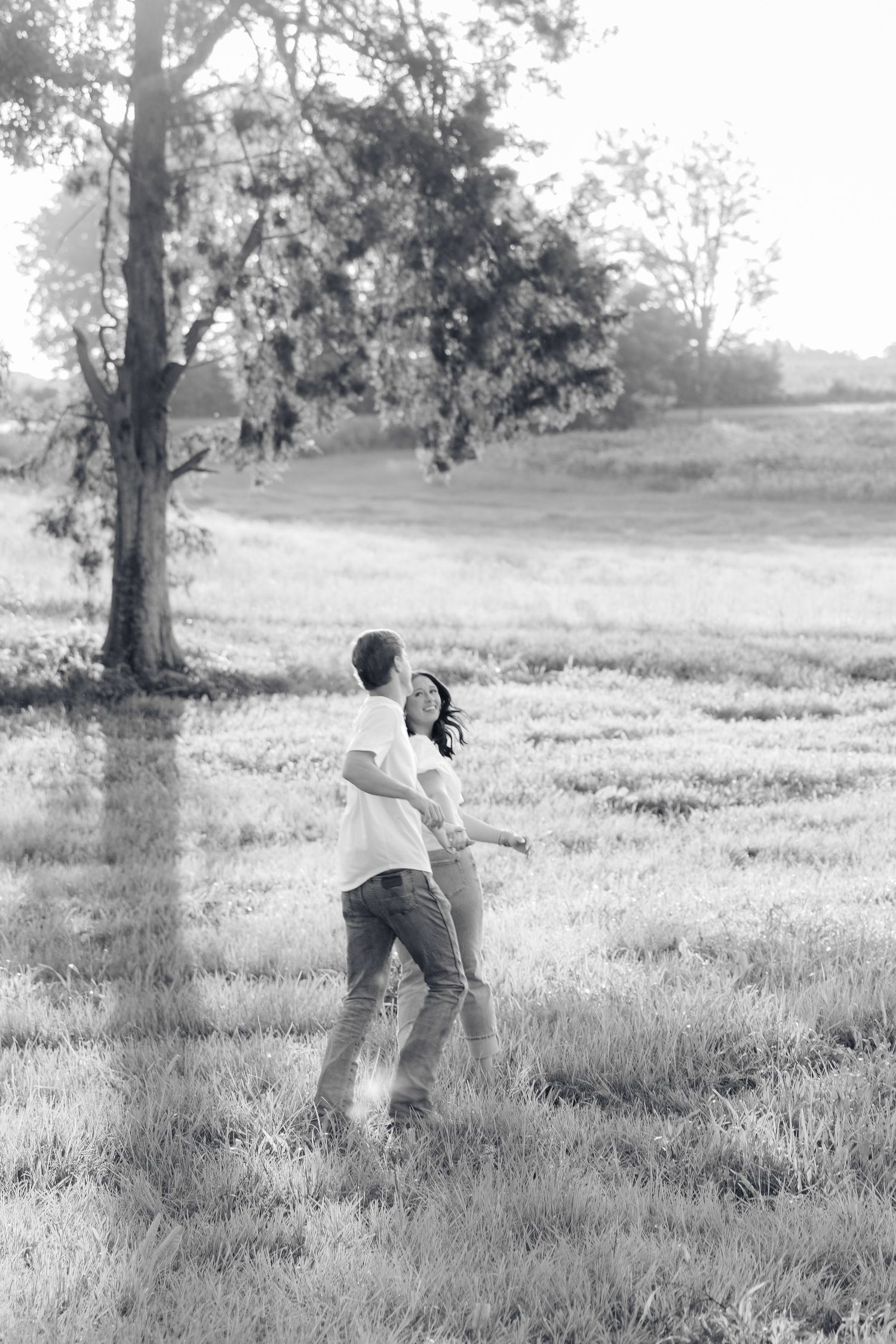 Romantic couple photos in a natural grass field setting with large trees at sunset.