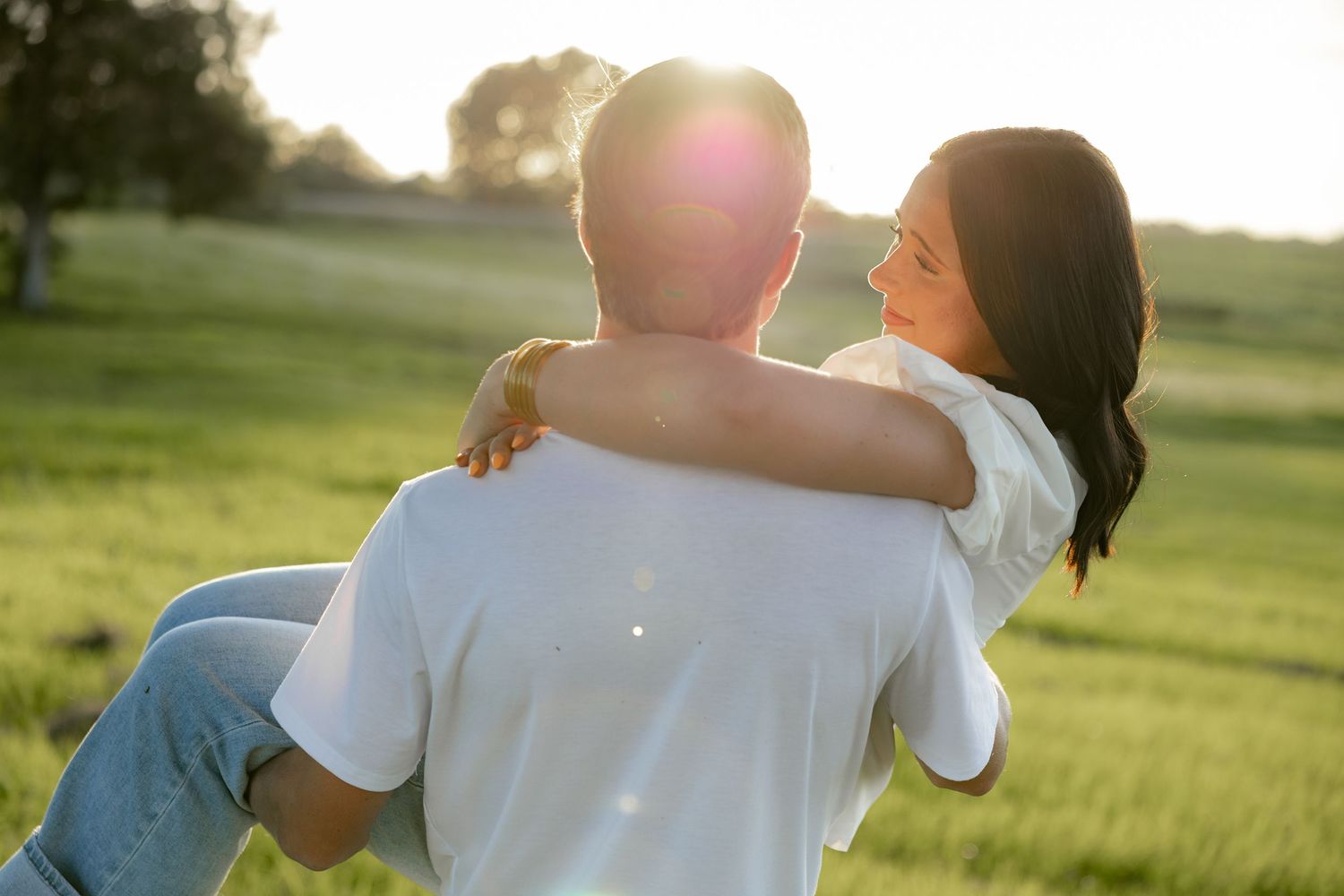 Romantic couple photos in a natural grass field setting with large trees at sunset.