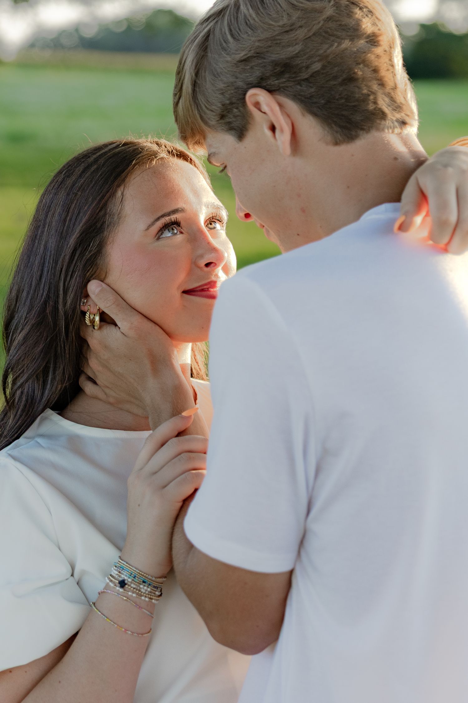 Romantic couple photos in a natural grass field setting with large trees at sunset.