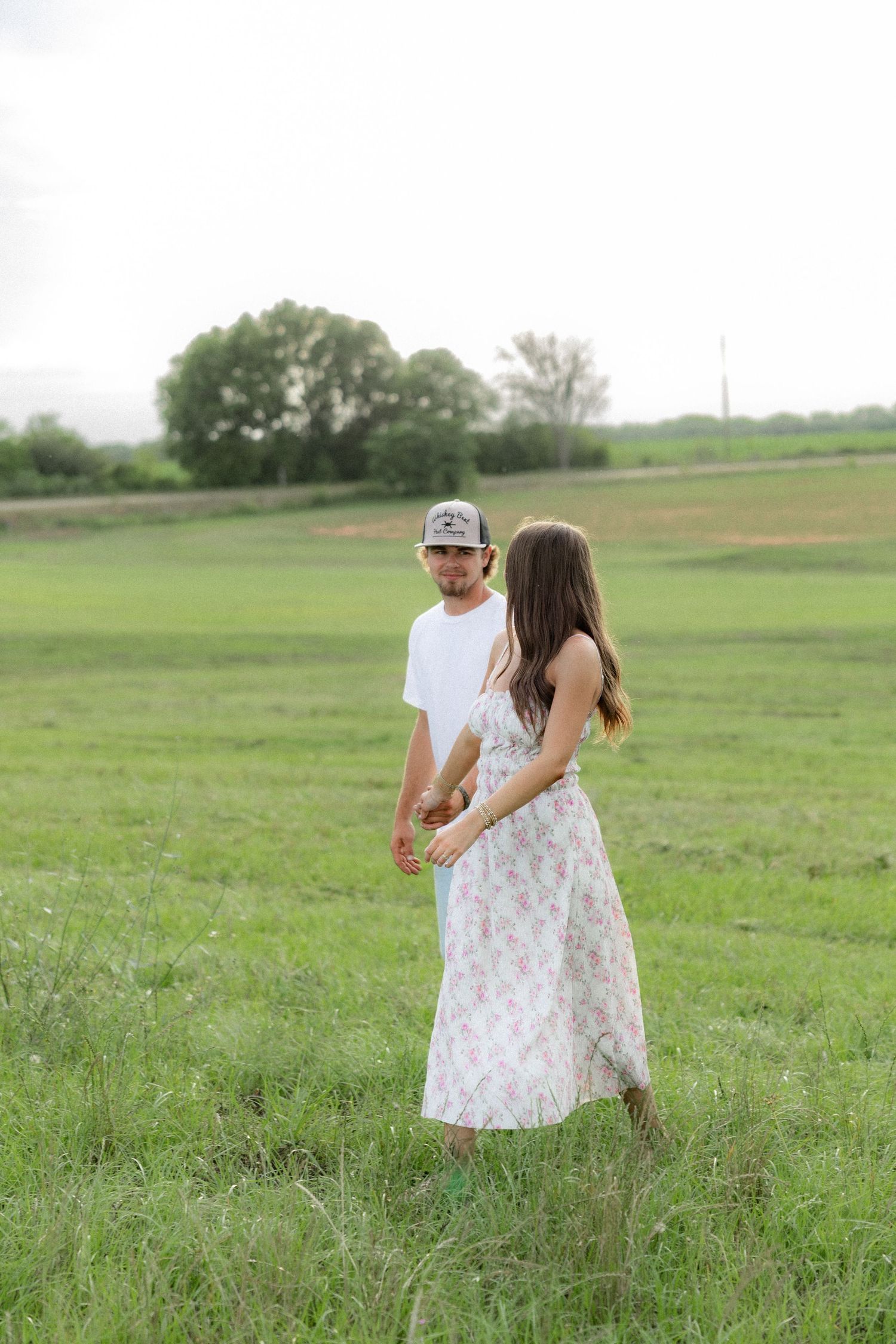 Romantic couple photos in a natural grass field setting with large trees at sunset.