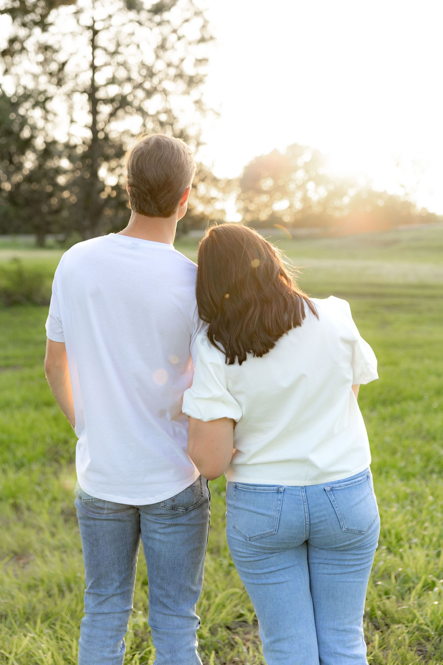 Romantic couple photos in a natural grass field setting with large trees at sunset.