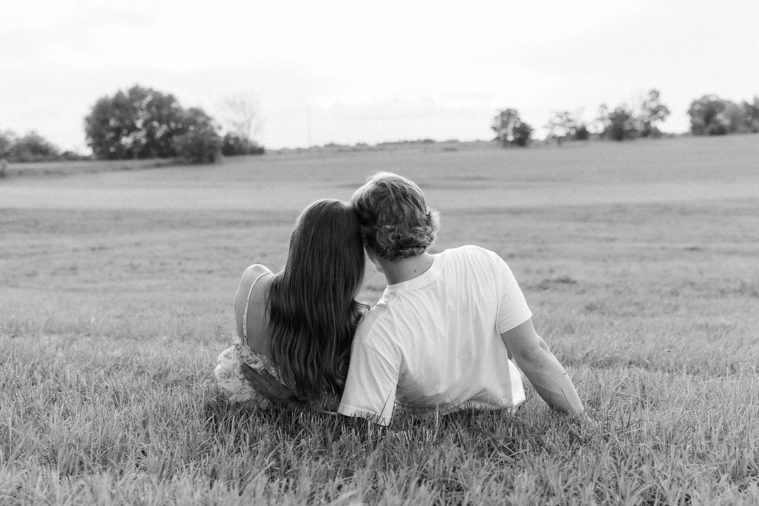 Romantic couple photos in a natural grass field setting with large trees at sunset.
